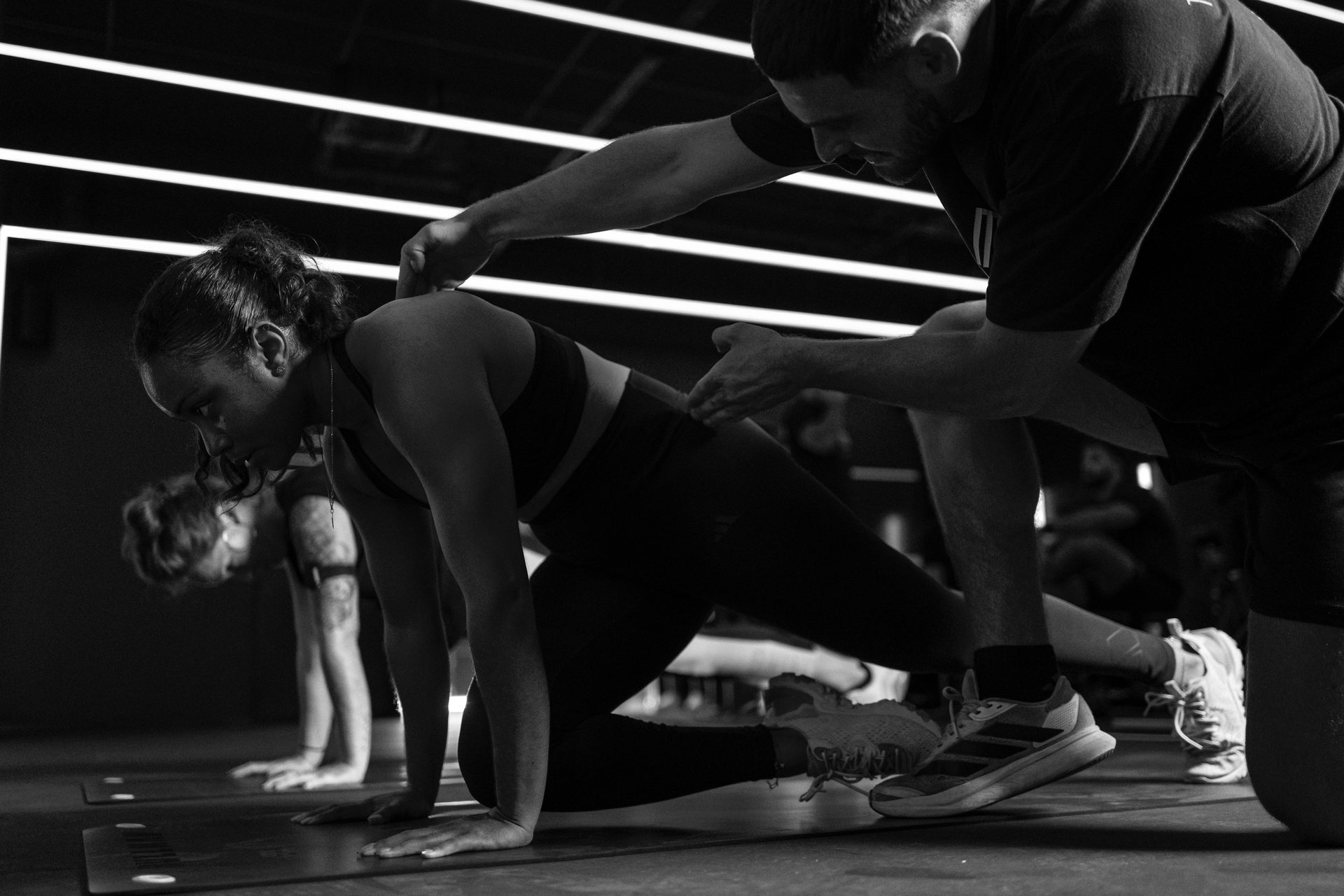 Un coach MONT NOIR ajuste la posture d'une adhérente pendant un exercice au sol